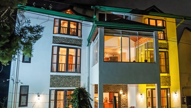 A multi-story building with a mix of brick and white walls, large windows, and outdoor lighting. - The Golden Legacy Hotel (Nuwara Eliya)