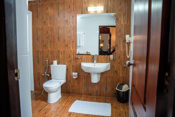 Un baño con pared de madera, un lavamanos blanco, un inodoro y un espejo.