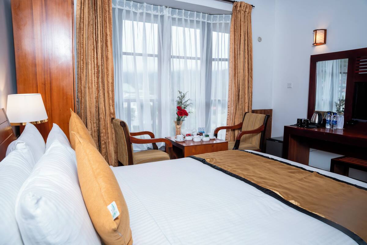 Een hotelkamer met een groot bed, een bureau met een lamp, een stoel en een kleine tafel met een bloemenvaas.