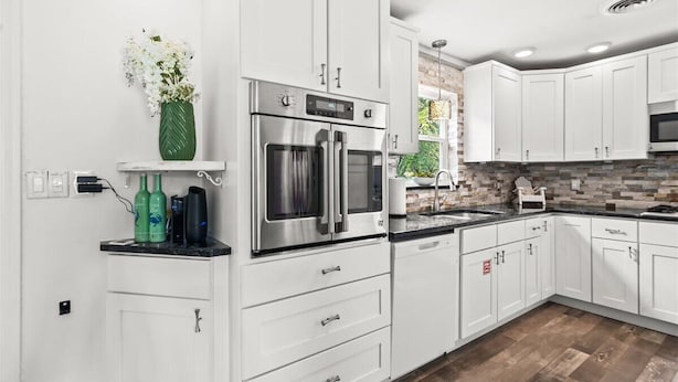 A modern kitchen with white cabinets, stainless steel appliances, and a black countertop. - Palm Paradise (Cocoa Beach)