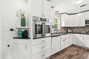 A modern kitchen with white cabinets, stainless steel appliances, and a black countertop. - Palm Paradise (Cocoa Beach)