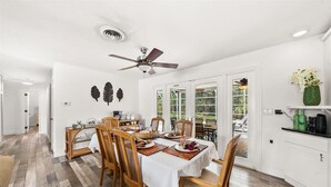 A dining area with a table set for four, wooden chairs, a ceiling fan, and a view through glass doors to an outdoor patio. - Palm Paradise (Cocoa Beach)