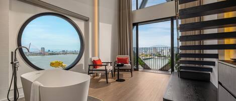 Un baño moderno con bañera, un ventanal redondo y vistas a un paisaje urbano.