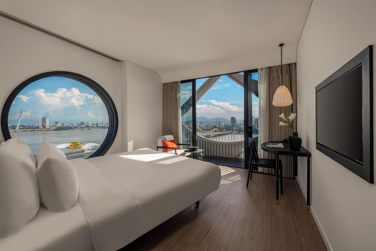 Une chambre d’hôtel moderne dotée d’un grand lit, d’un coin repas et offrant une vue sur le paysage urbain grâce à une grande fenêtre.