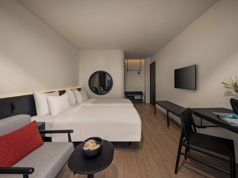 A modern hotel room with a bed, a sofa, a desk, and a TV.