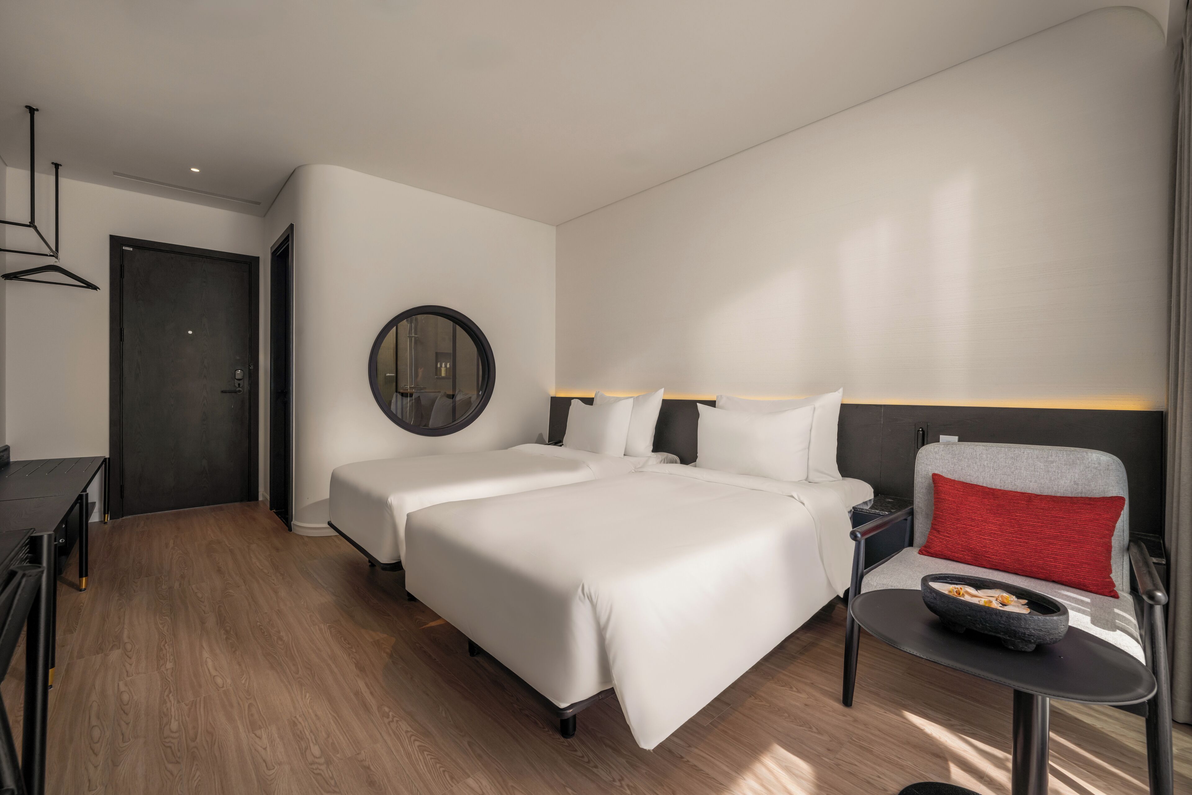 Una habitación de hotel con dos camas, un escritorio, una silla y una mesita con un bol.