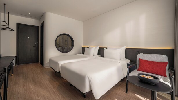 Een hotelkamer met twee bedden, een bureau, een stoel en een klein tafeltje met een schaal.