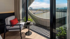 A modern room with a view of a cityscape, a chair with a red pillow, and a small table with a bowl. - Caro Premium Danang Hotel (Da Nang)