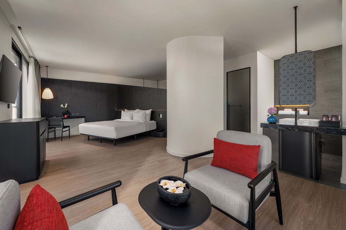 Une chambre d’hôtel moderne équipée d’un lit, d’un bureau, d’une chaise, d’une petite table agrémentée d’un vase de fleurs et d’un coin cuisine.