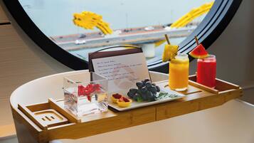 A table with a menu, fruit, and drinks, with a view of a bridge and vehicles through a window.