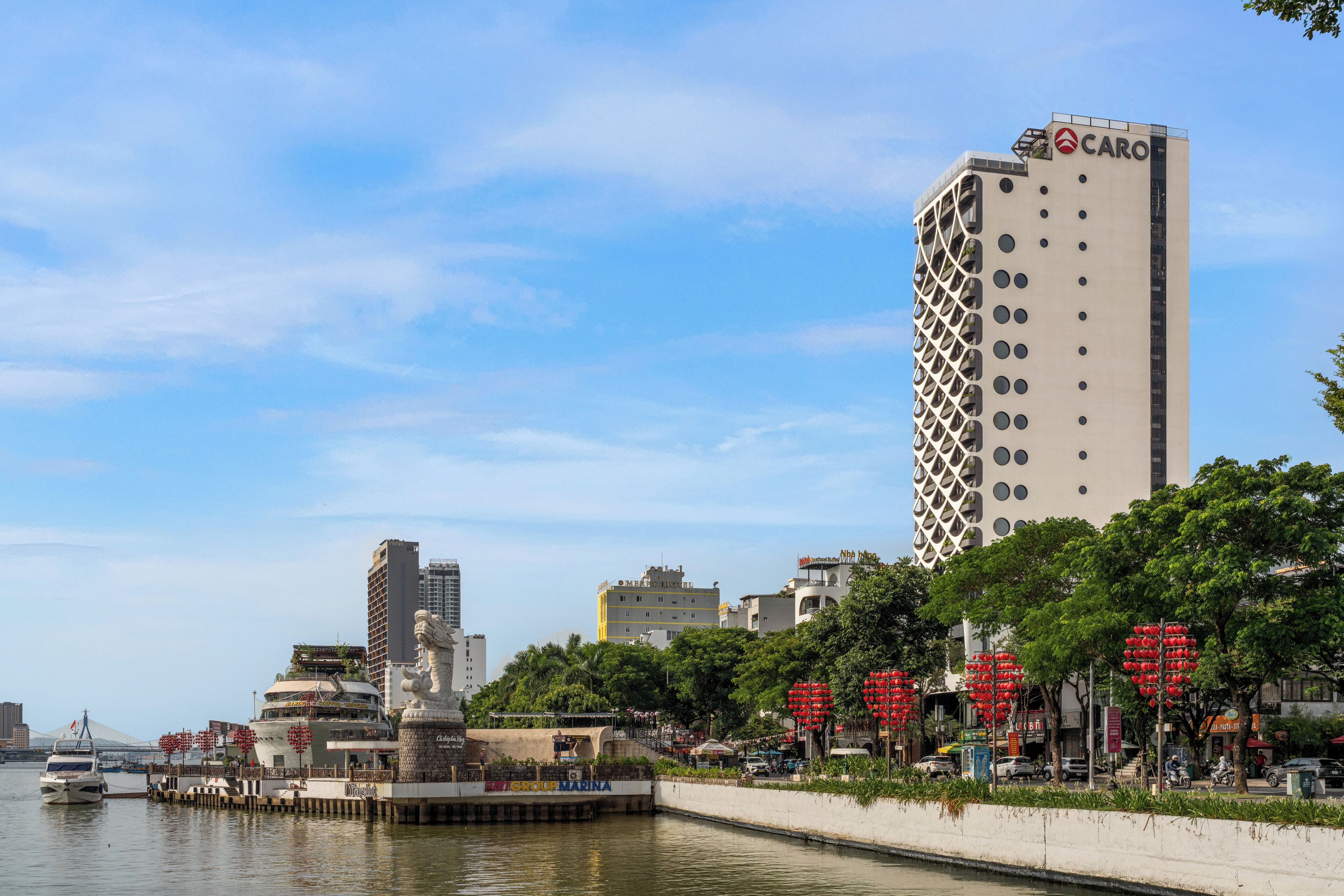 A marina with boats, a tall building with the name "CARO" on top, and a statue in the foreground.