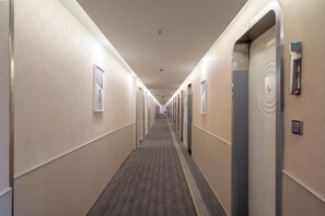 Un couloir d’hôtel avec des portes des deux côtés, un sol recouvert de moquette et un luminaire au plafond.