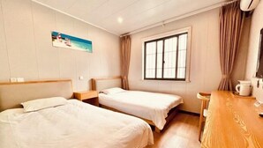 Une chambre d’hôtel avec deux lits, un bureau en bois, une fenêtre avec des rideaux et un tableau au mur.