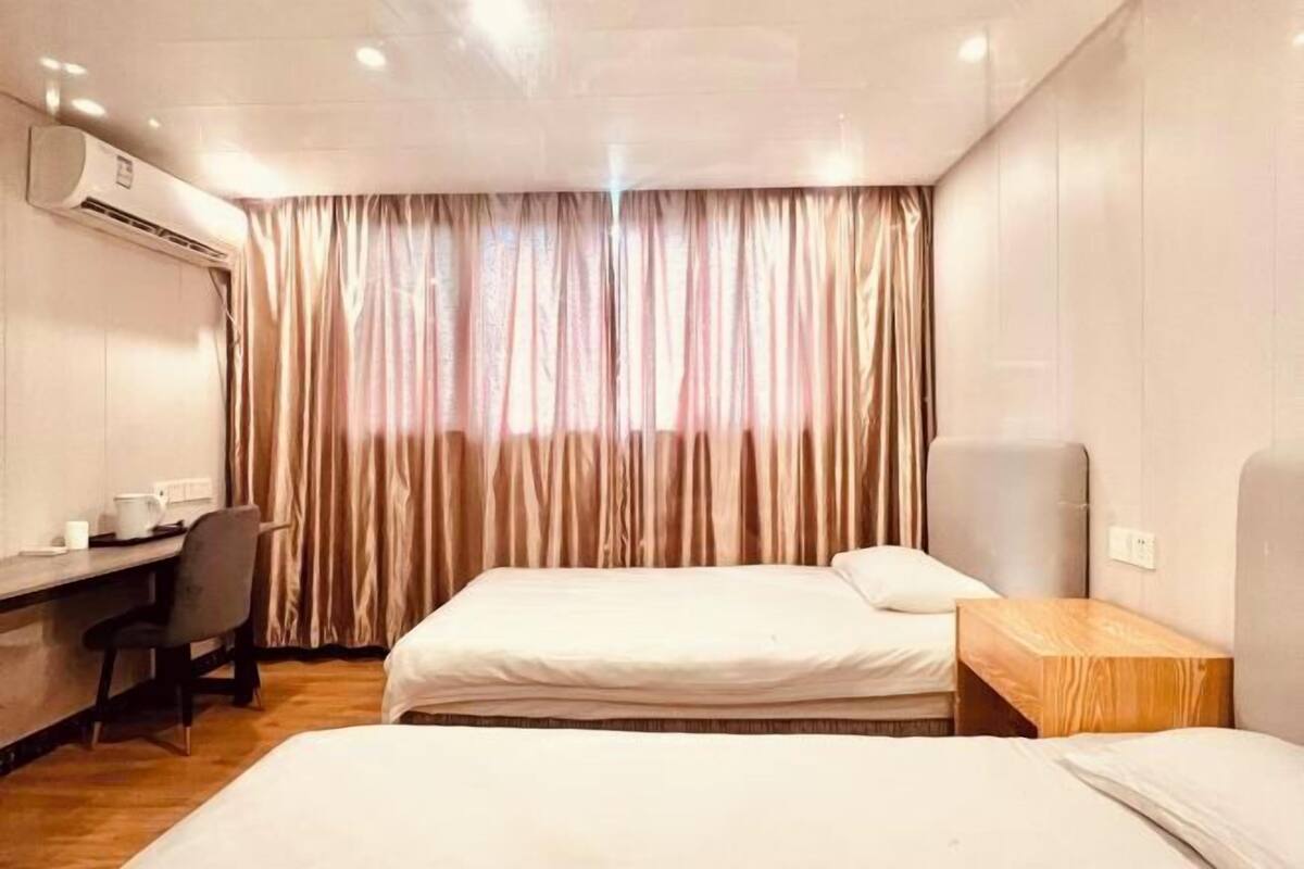 A hotel room with two beds, a desk, a chair, and an air conditioning unit.