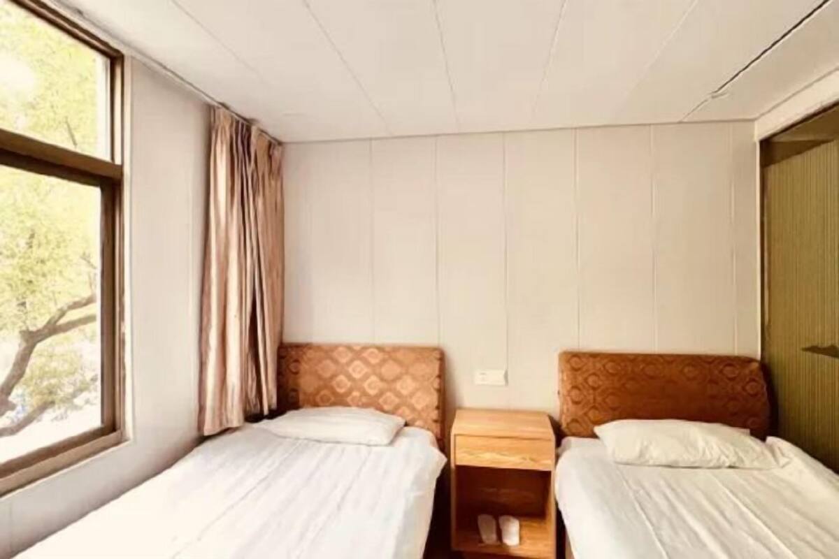 A room with two beds, a window with curtains, and a wooden nightstand with a shoe rack.