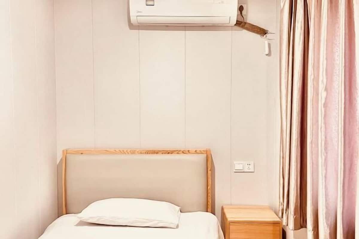A single bed with a wooden headboard, a bedside table, and an air conditioning unit mounted on the wall.