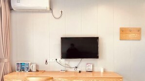 Une pièce comprenant un bureau en bois, un téléviseur fixé au mur, une prise de courant et une petite planche en bois.
