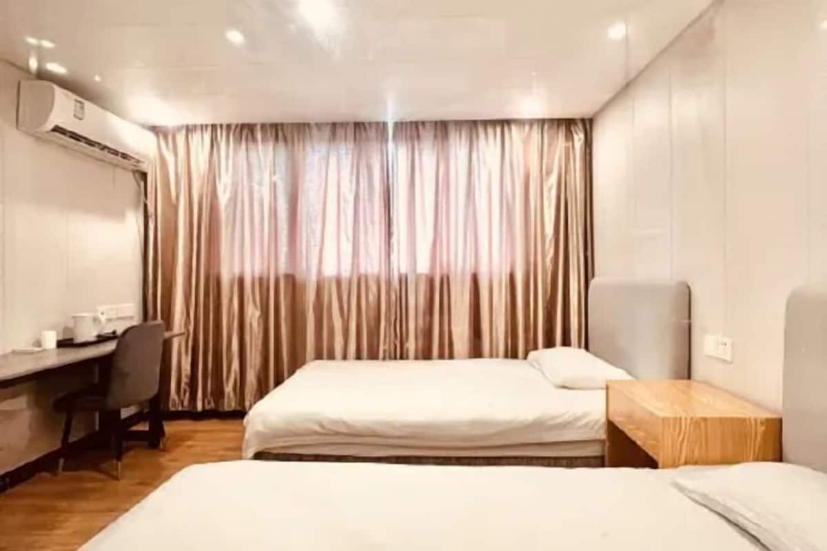 A hotel room with two beds, a desk, a chair, and an air conditioning unit.