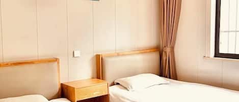 Habitación de hotel con dos camas individuales, una mesita de noche de madera, un cuadro de una playa y una ventana con cortinas.