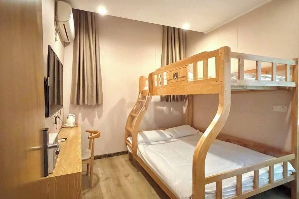 A bunk bed room with a desk and chair, a flat-screen TV, and a wall-mounted air conditioner.