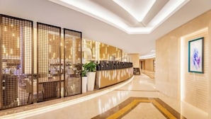 A modern hotel lobby with a curved reception desk, a large potted plant, and a framed artwork on the wall. - Ordos Taihua Langjing Hotel (Ordos)