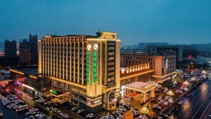 A multi-story hotel with a prominent clock tower, extensive parking, and a well-lit facade. - Ordos Taihua Langjing Hotel (Ordos)