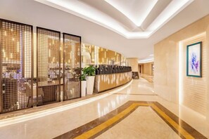Een hotellobby met een receptiebalie, een zithoek en een plant.