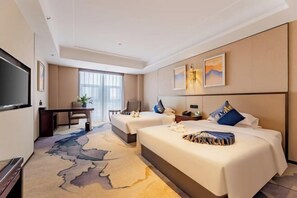 A hotel room with two beds, a desk, a TV, and a large window.
