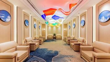 A hotel room with a long corridor, multiple seating areas, and a ceiling with a colorful light display.