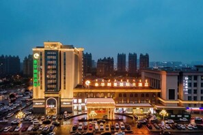 Un hotel con un letrero vertical llamativo, un estacionamiento y un paisaje urbano al fondo.