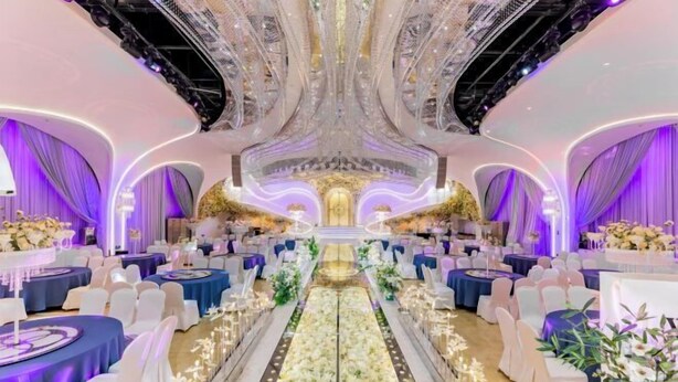 A grand ballroom with a central aisle, ornate ceiling, and rows of round tables with white chairs. - Ordos Taihua Langjing Hotel (Ordos)