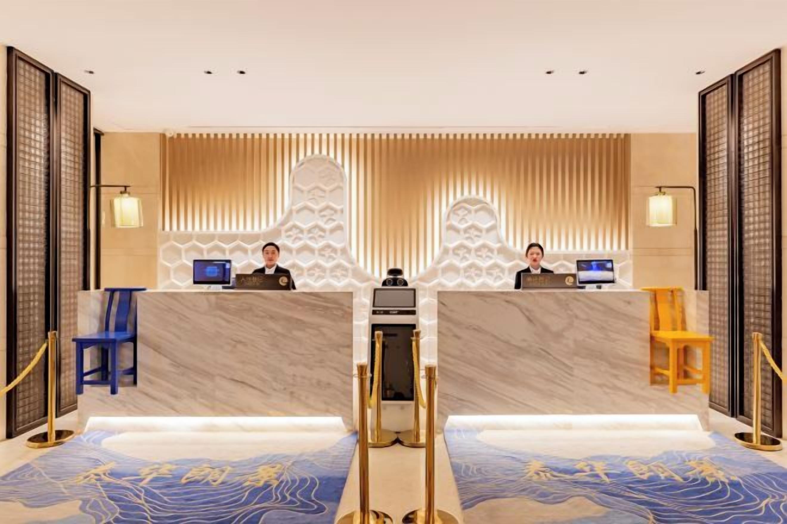 En hotellobby med en marmordisk, två receptionspersonal och en mönstrad matta.