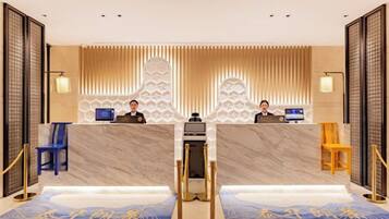 En hotellobby med en marmordisk, två receptionspersonal och en mönstrad matta.