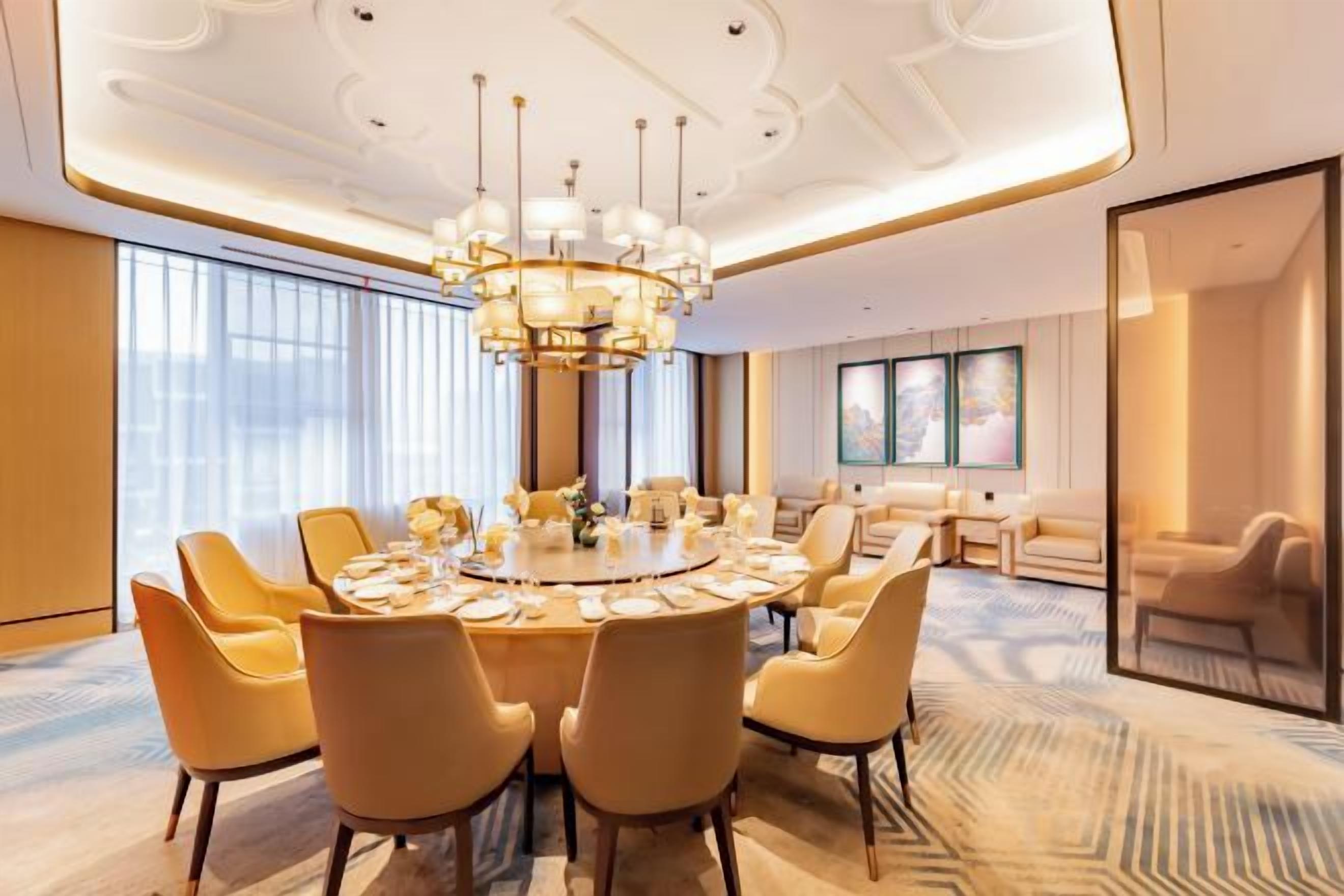A modern dining room with a round table, multiple chairs, and a chandelier.
