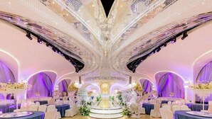 A grand hall with a central stage, surrounded by round tables with white chairs, and a decorative ceiling. - Ordos Taihua Langjing Hotel (Ordos)