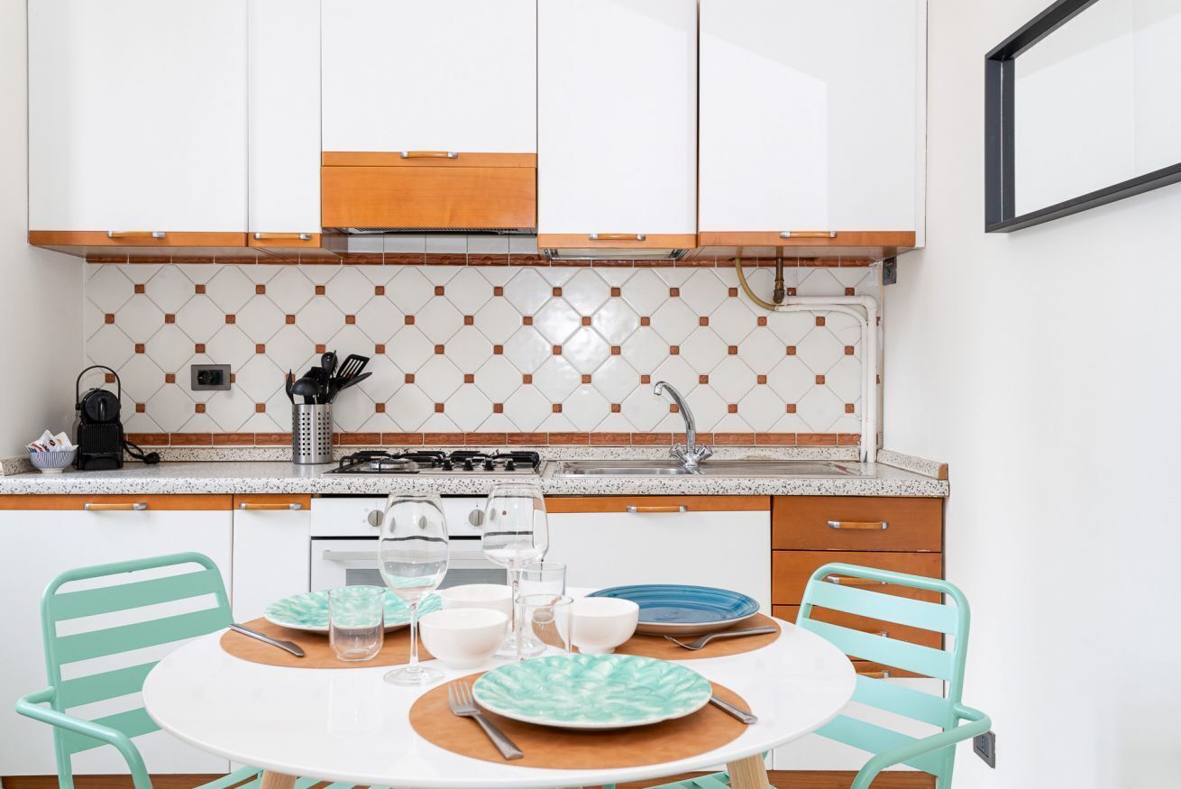 Una cocina compacta con armarios blancos, un backsplash de azulejos y una mesa redonda con sillas.