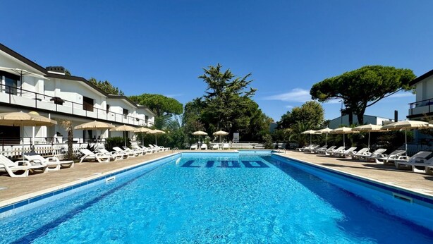 A swimming pool with lounge chairs and umbrellas, surrounded by buildings and trees.