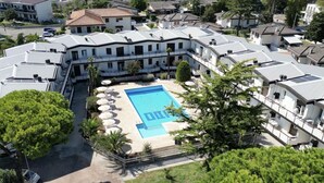 A residential building with a swimming pool surrounded by lounge chairs and a well-maintained garden. - Family Apartments Villaggio Lido B3 - Carraro Immobiliare Jesolo (Cavallino-Treporti)
