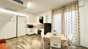 A compact kitchen with modern appliances, a dining area with a table and chairs, and a small seating area with a sofa. - Family Apartments Villaggio Lido B3 - Carraro Immobiliare Jesolo (Cavallino-Treporti)