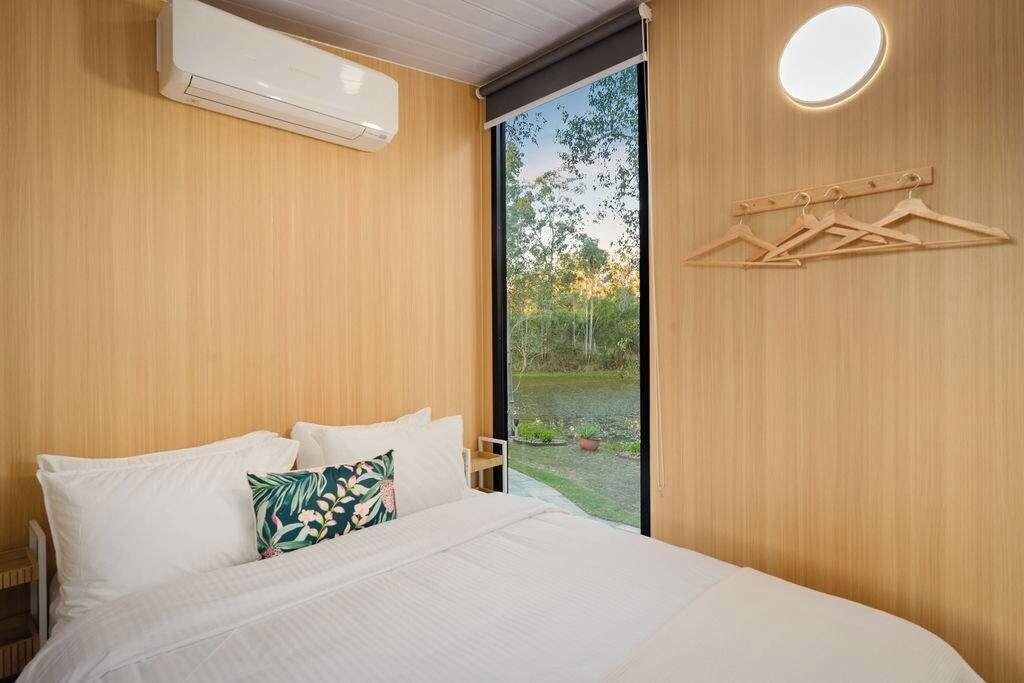 Een slaapkamer met een bed, een raam en een luchtverkoeler aan de muur.