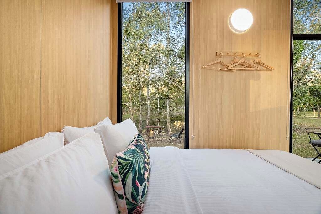 A bedroom with a large bed, a view of trees, and a wooden wall with a hanging light fixture.