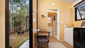 A modern kitchen with a wooden interior, a dining area with a bench, and a view of the outdoors. - JJJ's Ranch Farm 1 by Tiny Away (South Kolan)