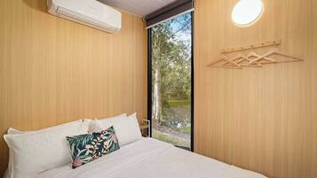 Ein Schlafzimmer mit einem Bett, Kissen, einer Klimaanlage, einer Holzwand, einem Fenster und einer Wandleuchte.