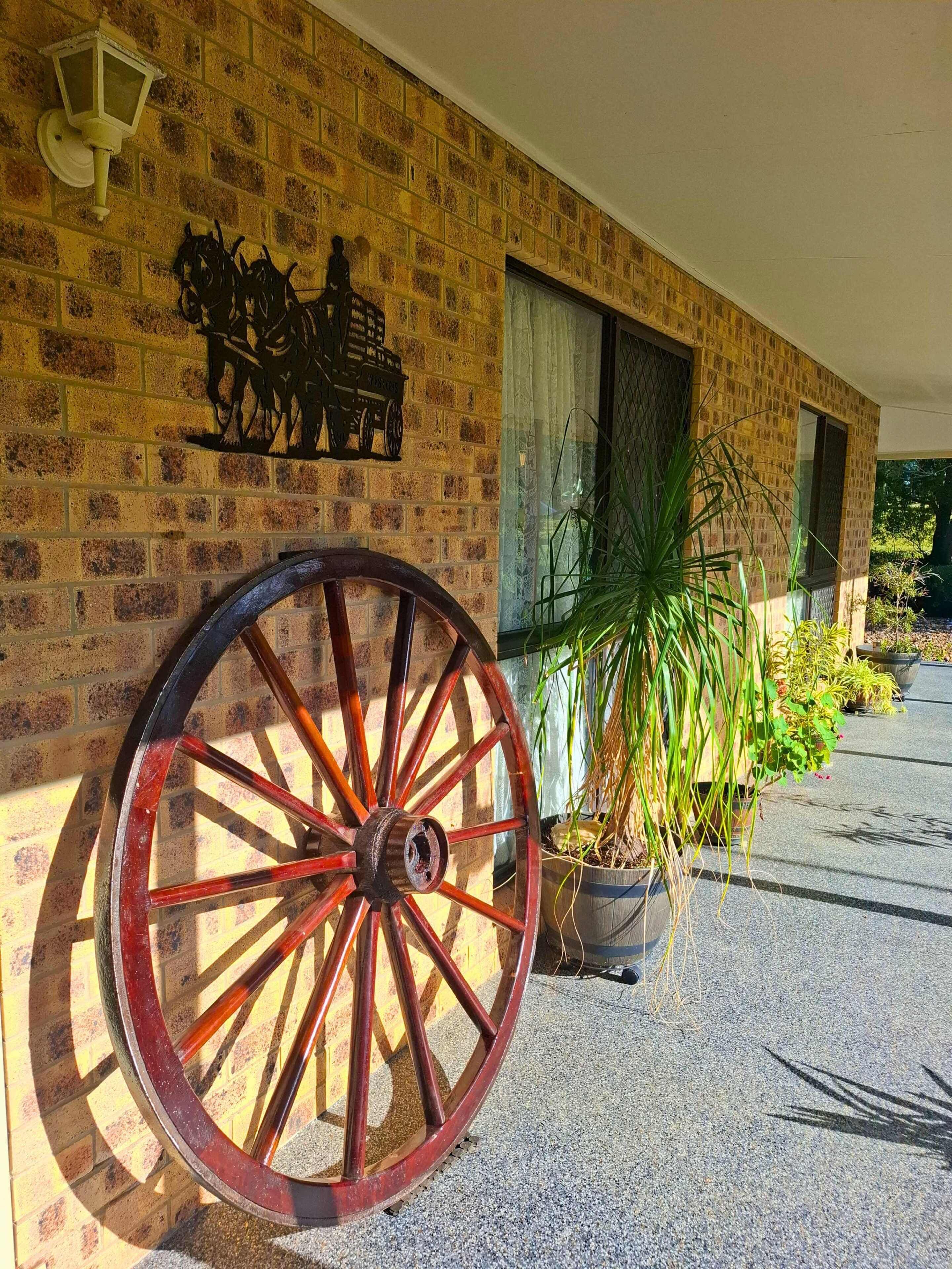 Un bâtiment doté d’une grande roue en bois, d’un mur en briques, d’un élément décoratif en métal et de plantes en pot.