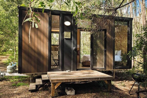 A wooden cabin with a sliding door, a small outdoor seating area, and a view of the surrounding forest.