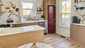 A modern kitchen with marble countertops, wooden cabinets, a central island, and a red refrigerator.