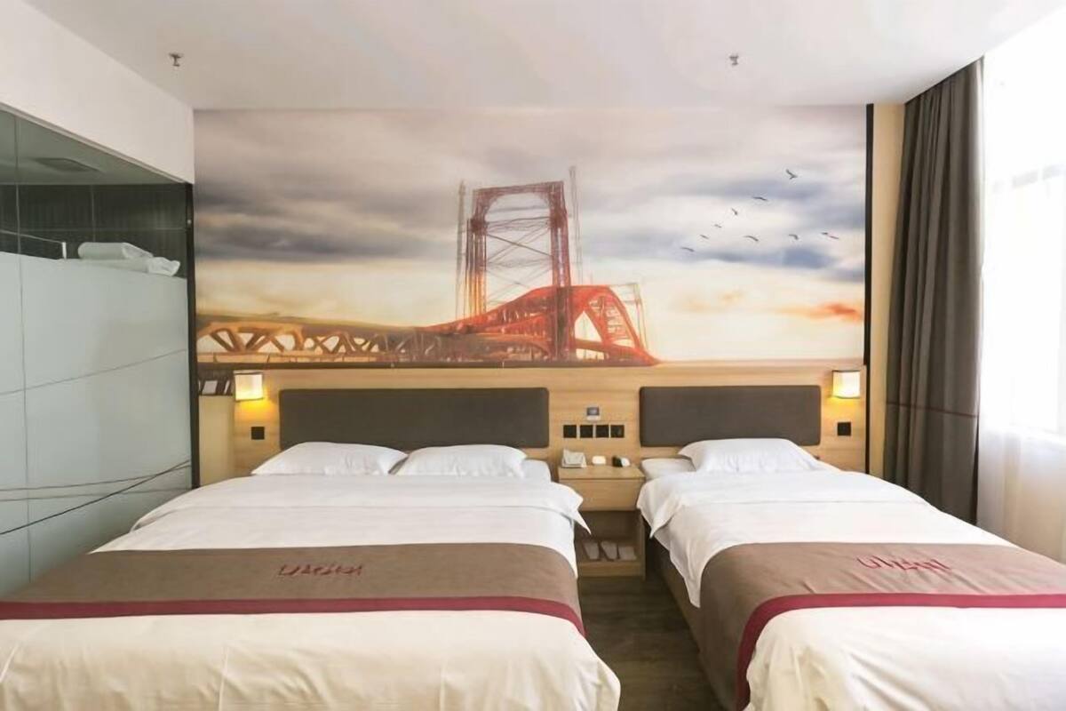 A hotel room with two beds, a large mural of a bridge, and a view of the sky.