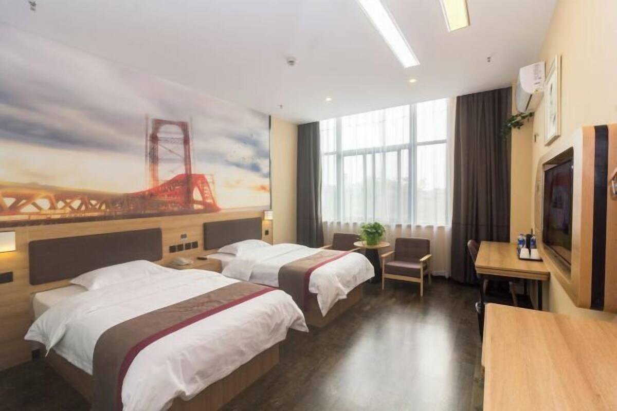 A hotel room with two beds, a desk, a chair, a TV, and a large window.