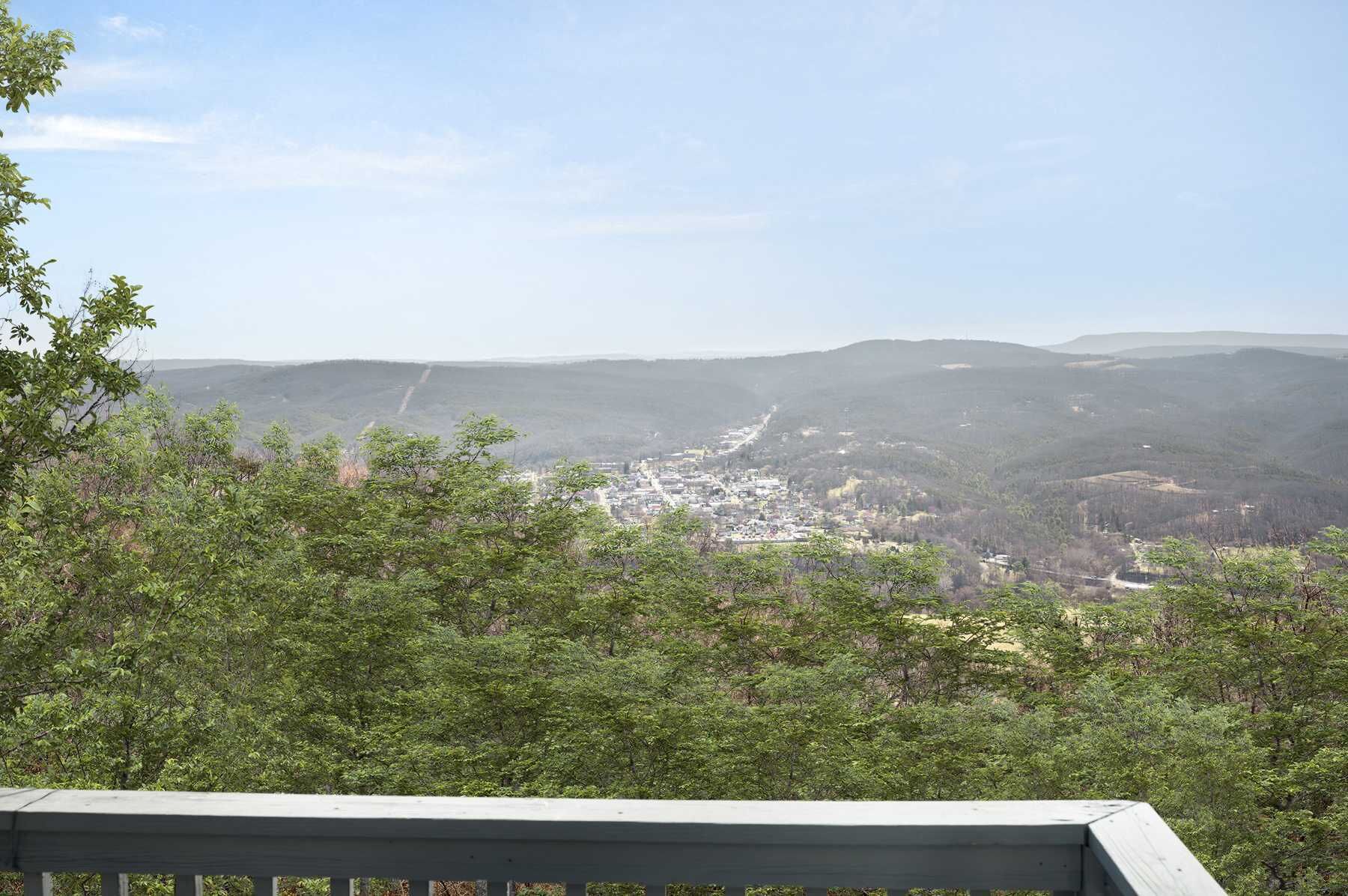 Vista desde un punto elevado que domina un pueblo situado en un valle, rodeado de colinas boscosas.