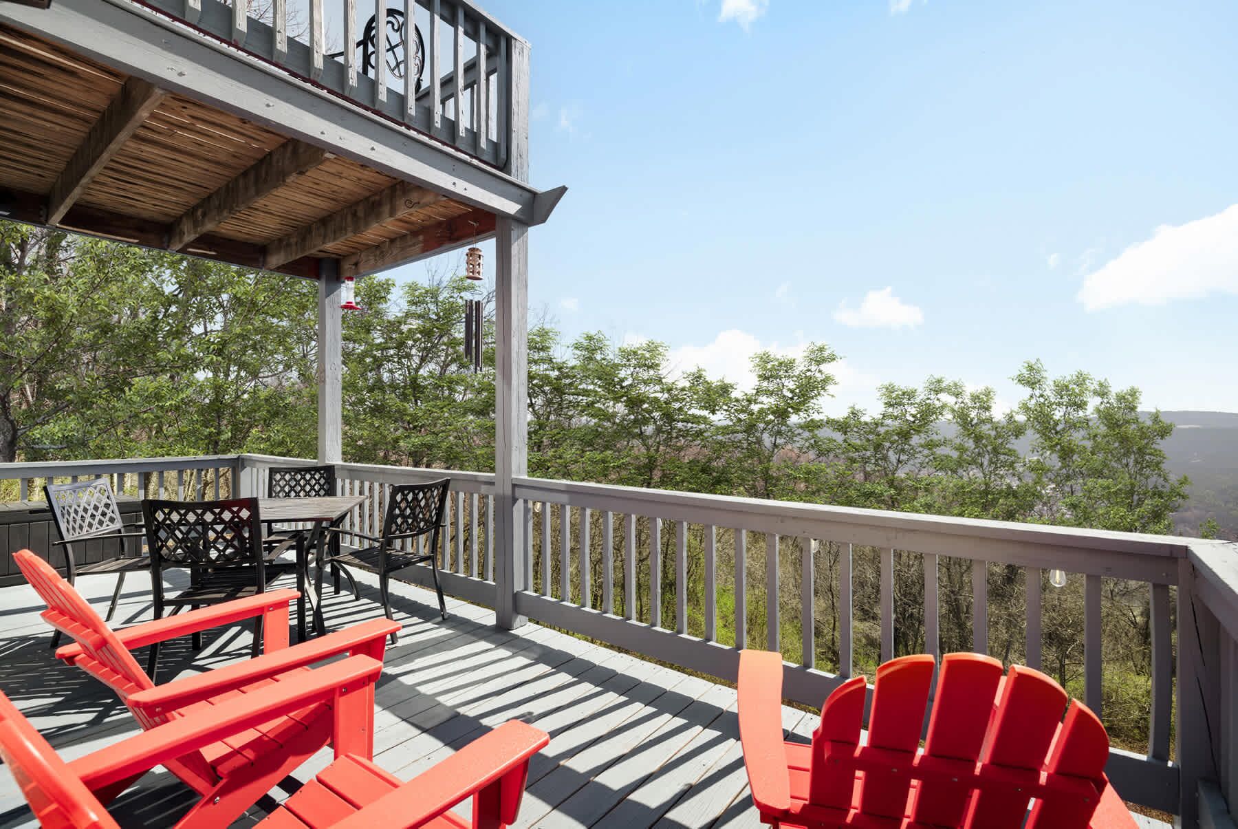 Une terrasse en bois avec des sièges d’extérieur, notamment des fauteuils Adirondack rouges et une table, donnant sur une zone boisée.